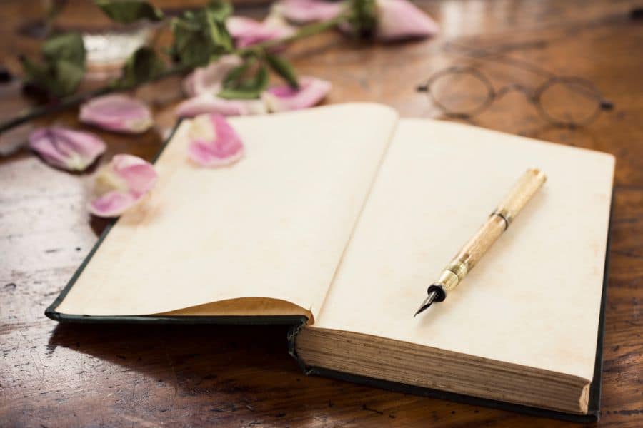 open journal with blank page and a pen on a wooden table with pink flowers. 